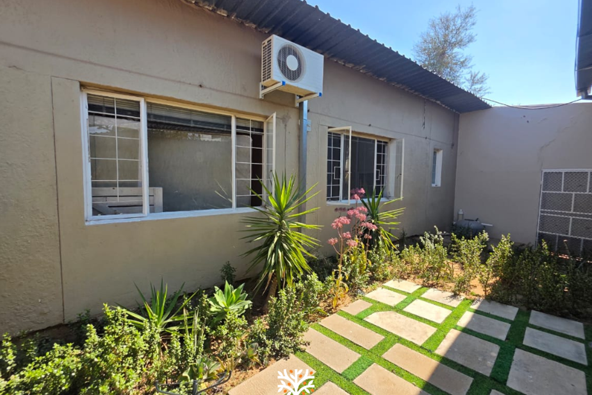 Rear exterior view of the property featuring a paved garden path, established landscaping, and an external air conditioning unit mounted on the wall.