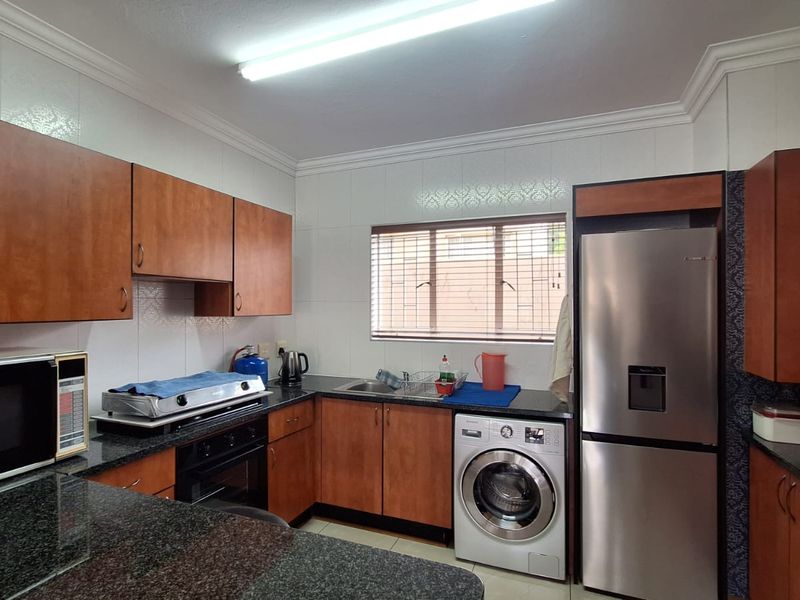 A functional kitchen featuring wood-finish cabinetry, granite countertops, a built-in oven with gas hob, and an integrated washing machine.