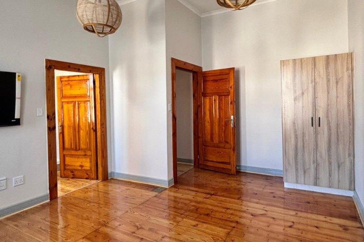 A bright bedroom featuring polished wooden flooring, built-in cabinetry, and two wooden door frames leading to adjacent rooms.