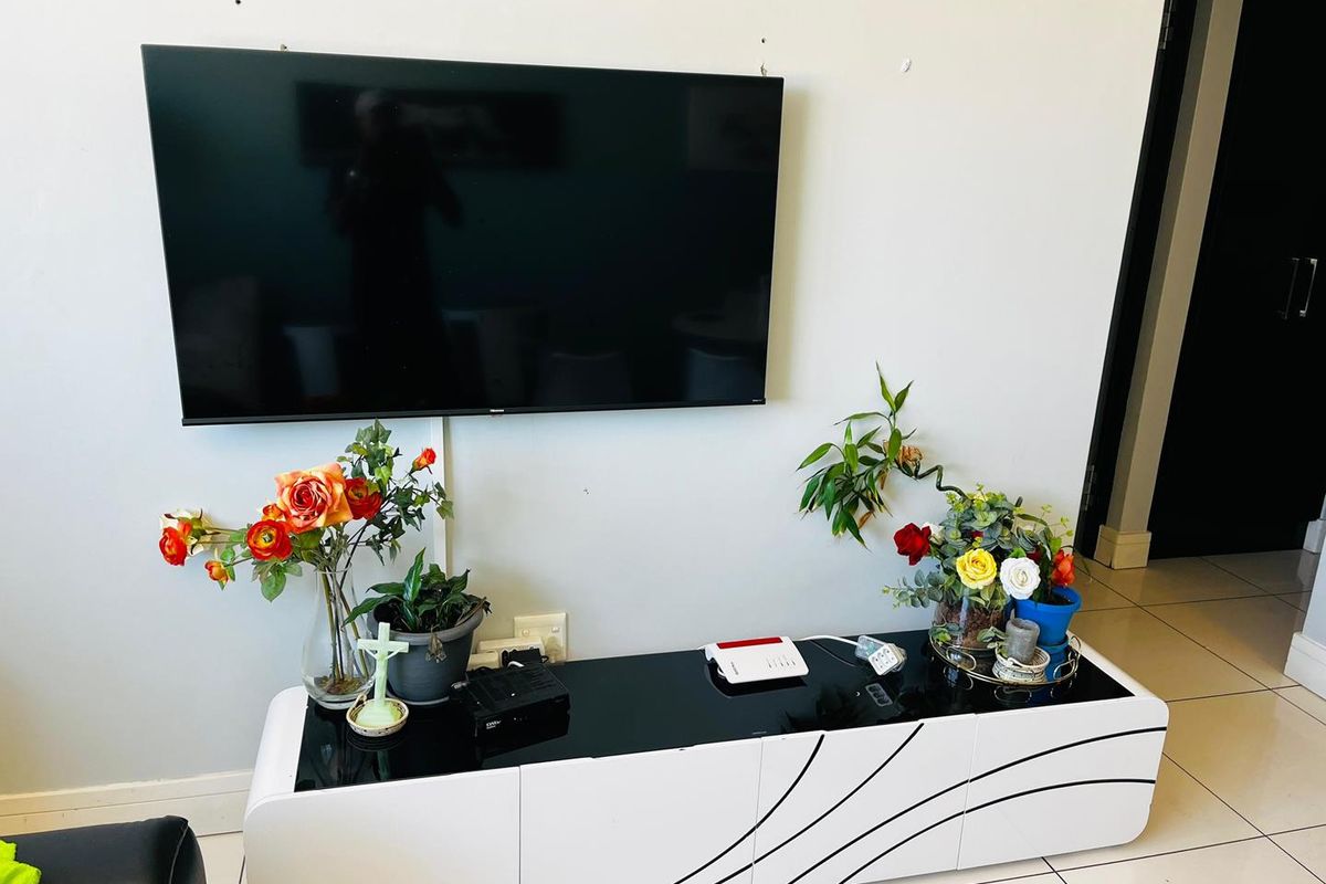 A living room area featuring tiled flooring and a wall-mounted television with visible cable management.