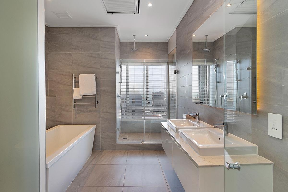Modern bathroom featuring a double vanity, a deep soaking bathtub, and a glass-enclosed walk-in shower with contemporary grey tiling throughout.