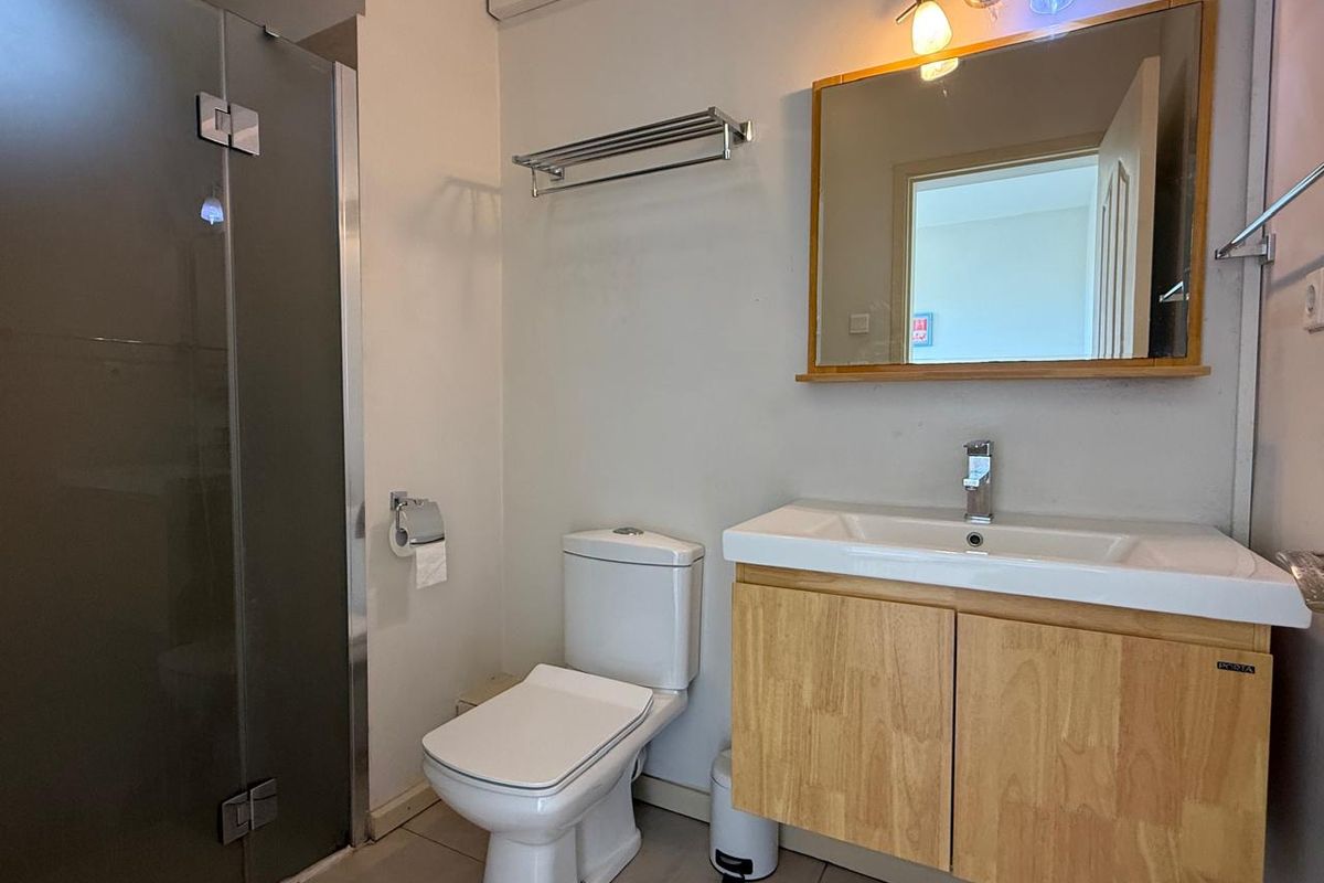 A functional bathroom featuring a vanity with a wooden cabinet, a wall-mounted mirror, a toilet, and a glass-enclosed shower area.