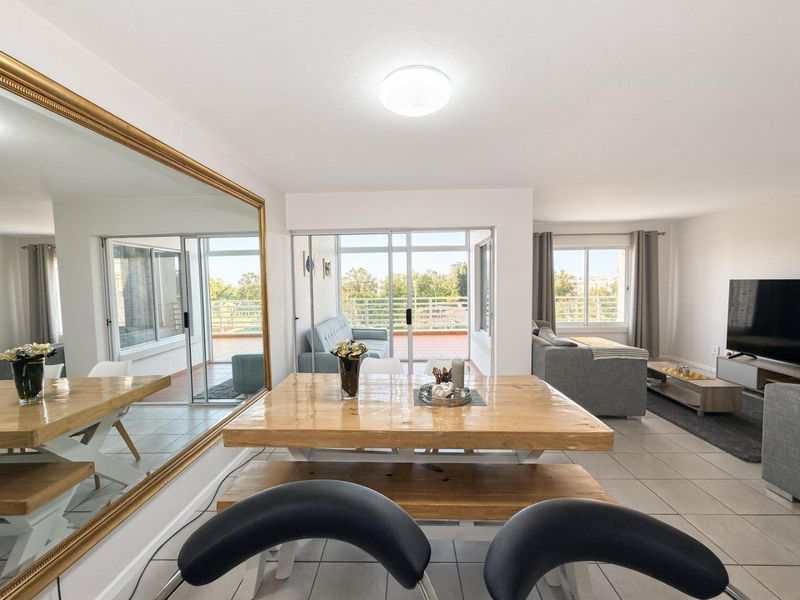 Spacious open-plan living and dining area featuring tiled flooring, large sliding glass doors leading to a balcony, and a prominent wall-mounted mirror.