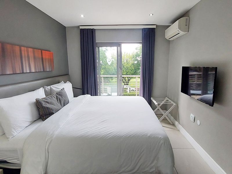 A well-maintained bedroom featuring tiled flooring, recessed lighting, a wall-mounted air conditioning unit, and a sliding glass door providing access to a balcony.