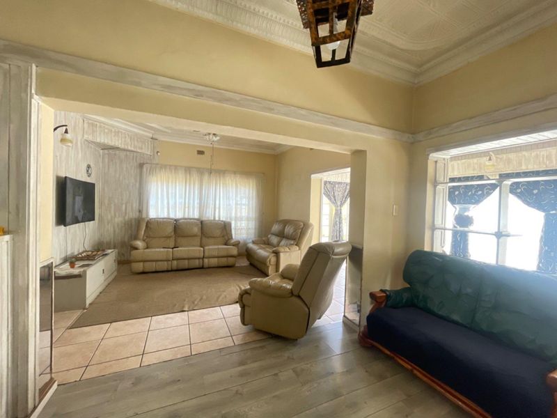 Spacious living area featuring a mix of tiled and laminate flooring, ornate ceiling detailing, and large windows allowing for natural light.