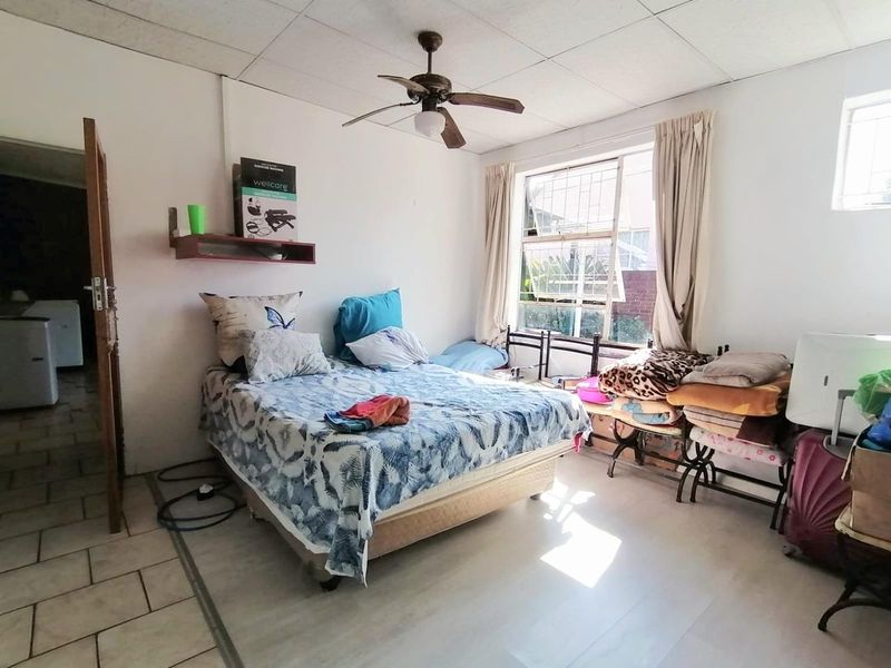 A bedroom featuring a ceiling fan, tiled flooring, and security bars on the window, offering a functional space with potential for cosmetic updates.