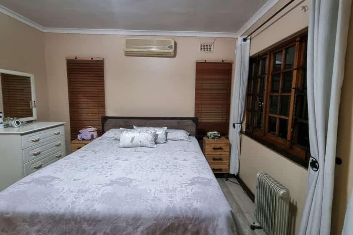 A functional bedroom featuring tiled flooring, timber-framed windows with matching blinds, and a wall-mounted split-system air conditioning unit.