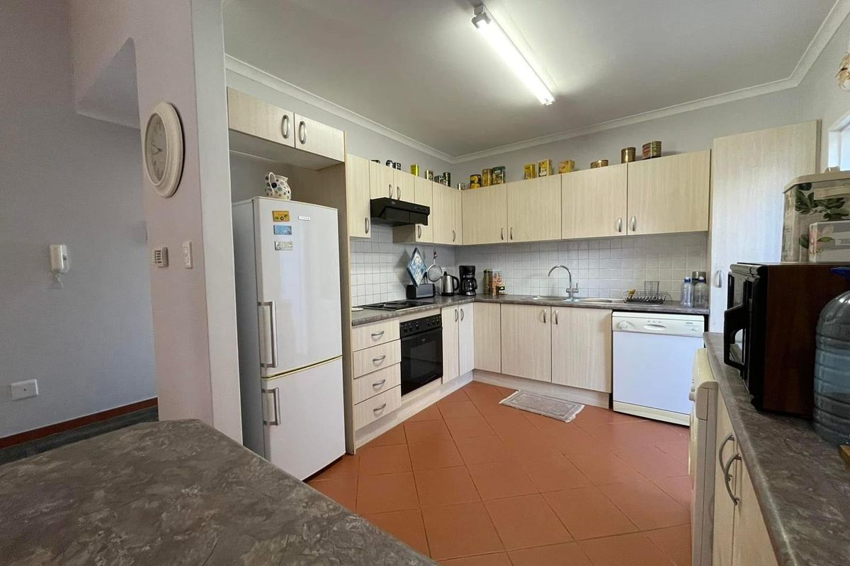 Functional kitchen featuring light wood-look cabinetry, tiled backsplash, built-in oven, hob, and extractor fan with terracotta floor tiling.