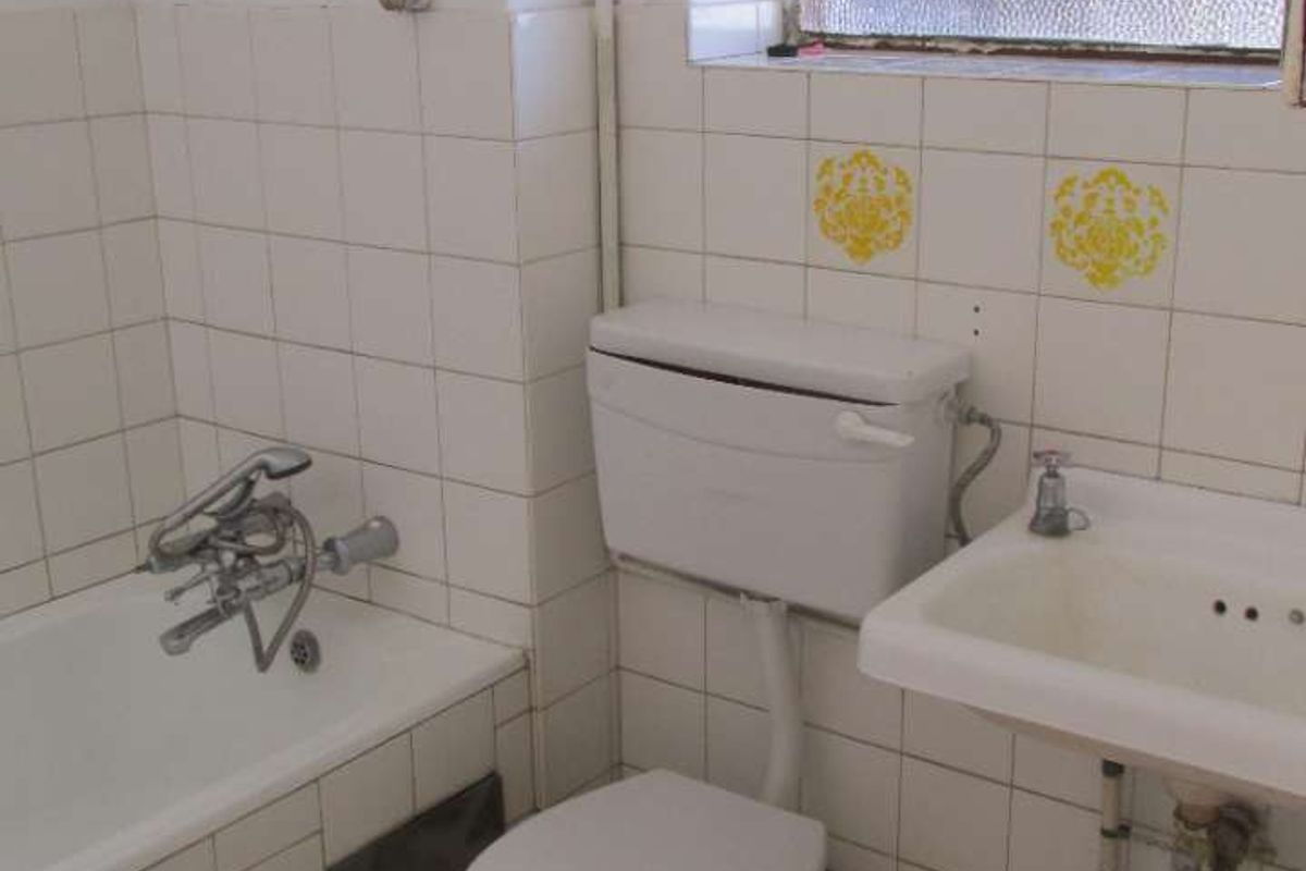 A dated bathroom featuring a standard bathtub, pedestal basin, and toilet with original wall tiling and exposed plumbing fixtures.