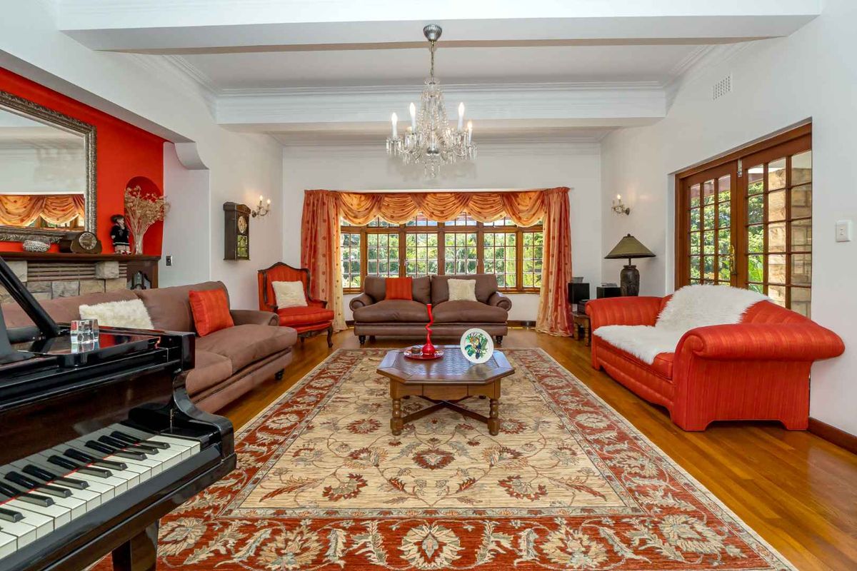Spacious living room featuring polished timber flooring, decorative ceiling beams, a crystal chandelier, and classic French doors leading to the exterior.