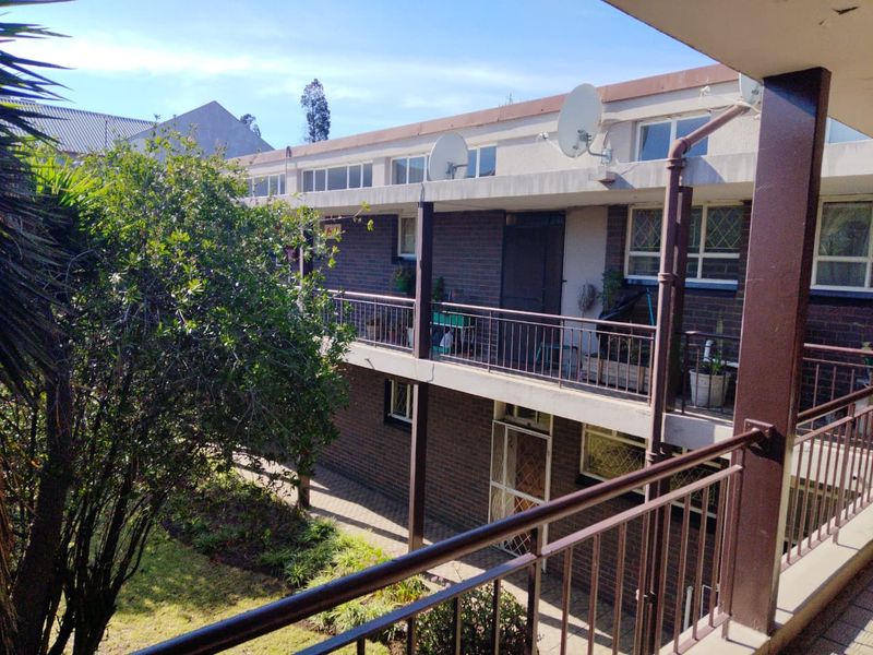 Exterior view of a multi-story townhouse complex featuring brick facade, metal balcony railings, and a shared garden area.