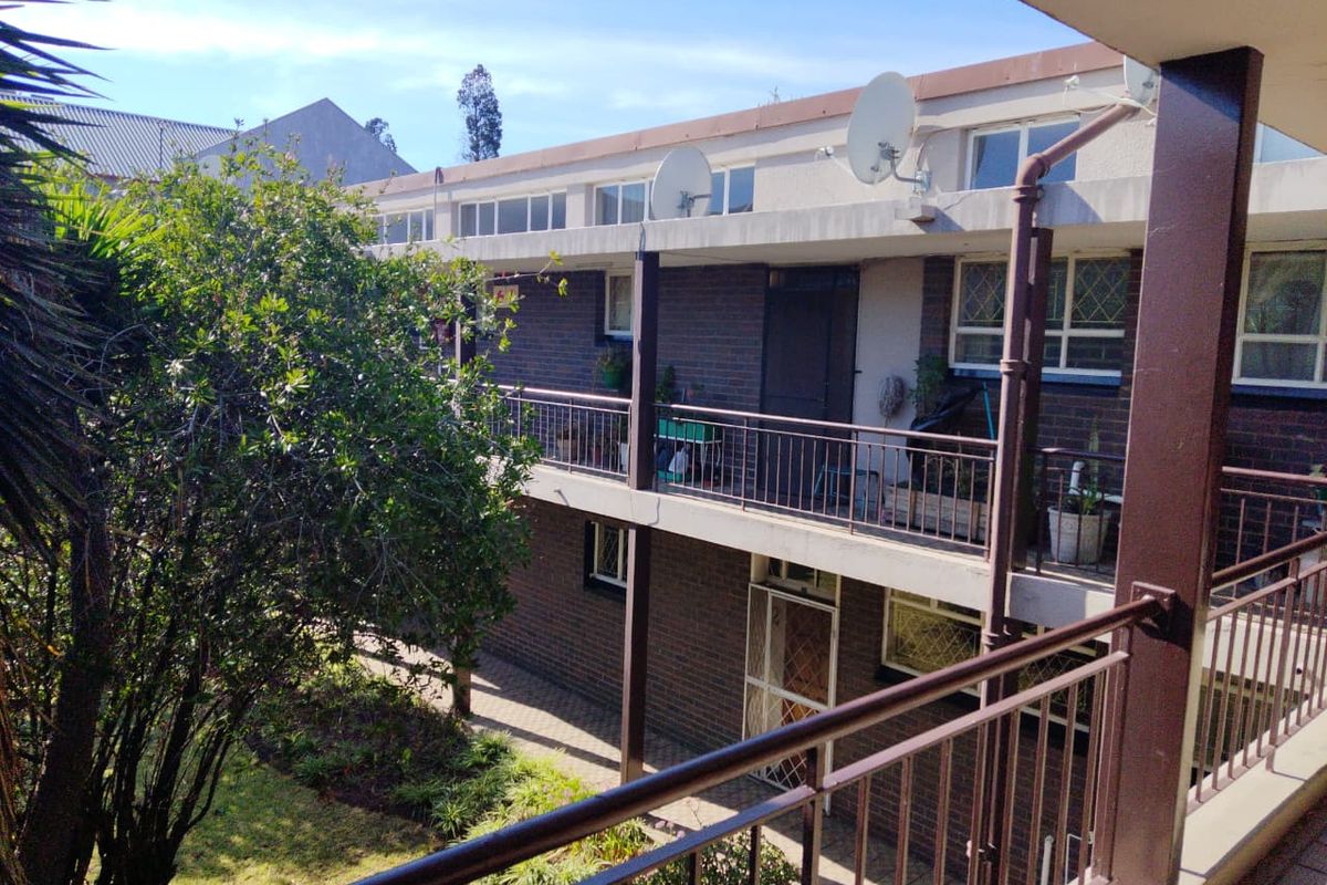 Exterior view of a multi-story townhouse complex featuring brick facade, metal balcony railings, and a shared garden area.
