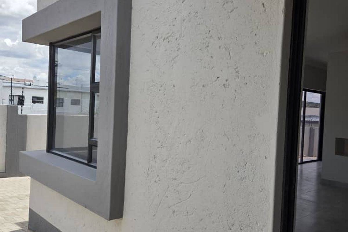 Exterior view of a modern home featuring textured plaster walls, a framed window detail, and paved outdoor area.