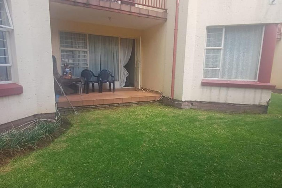 Rear view of the apartment featuring a ground floor tiled patio, a first-floor balcony with metal railing, and a private garden area.