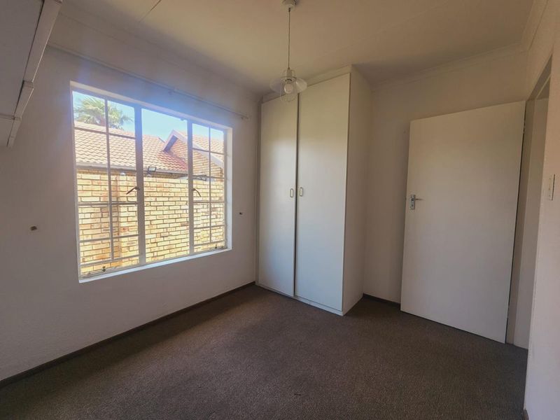 A clean, empty bedroom featuring neutral walls, carpeted flooring, and a built-in wardrobe, offering a blank canvas for personalization.