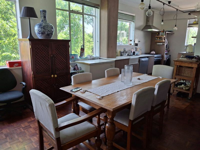 An open-plan living and dining area featuring warm parquet flooring, large windows for natural light, and a functional kitchen with a farmhouse sink.
