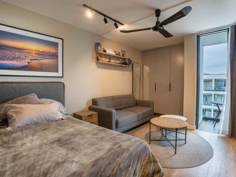 A well-maintained bedroom featuring built-in cupboards, modern track lighting, a ceiling fan, and direct access to a private balcony through a sliding glass door.