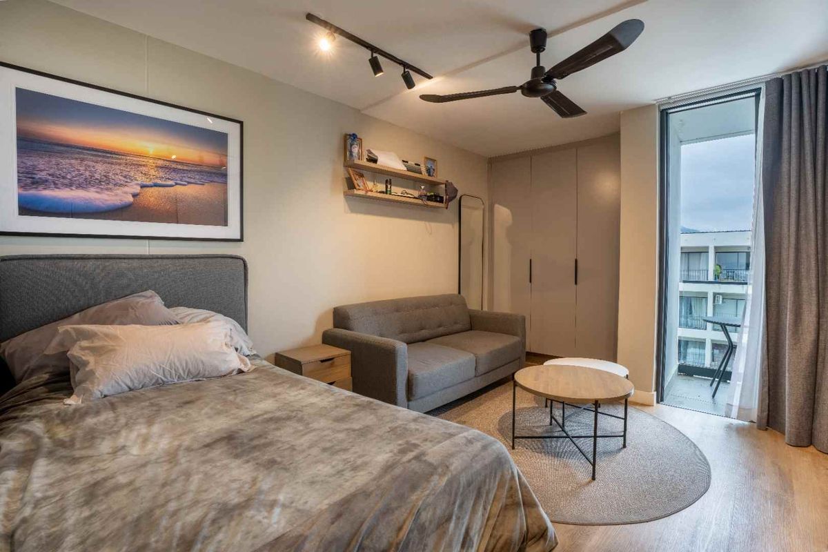 A well-maintained bedroom featuring built-in cupboards, modern track lighting, a ceiling fan, and direct access to a private balcony through a sliding glass door.
