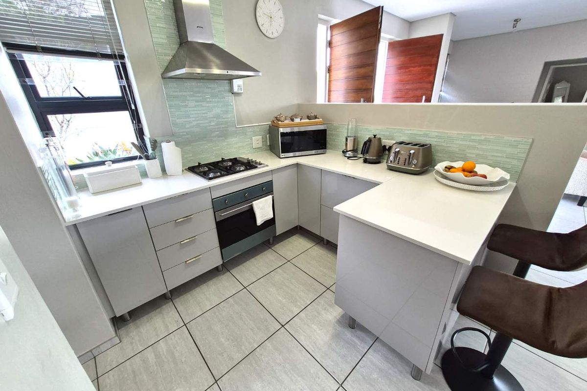 Modern kitchen featuring light grey cabinetry, quartz countertops, a gas hob, stainless steel extractor fan, and a stylish glass mosaic backsplash.