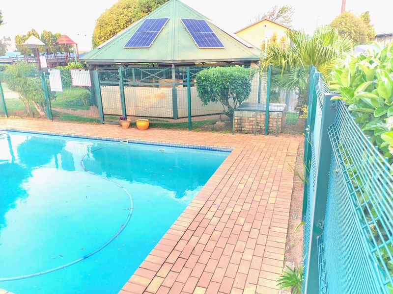 Outdoor pool area featuring a swimming pool, brick paved surround, mesh perimeter fencing, and a gazebo equipped with solar panels.