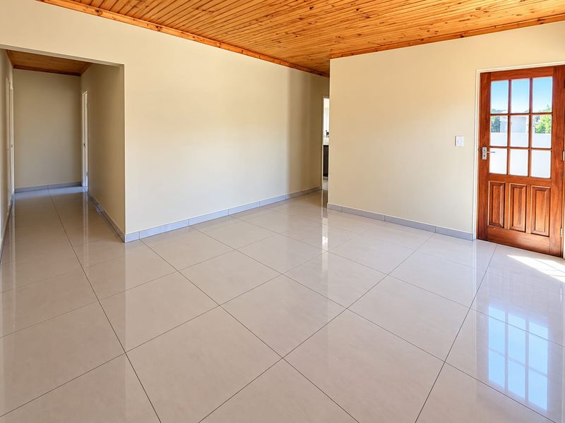 Spacious, empty living area featuring polished porcelain floor tiles and a warm timber tongue and groove ceiling, leading to an entrance door.