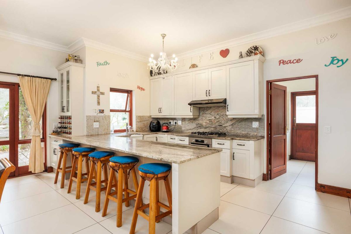 A well-maintained kitchen featuring granite countertops, built-in cabinetry, a gas hob, extractor fan, and a breakfast bar island with tiled flooring.