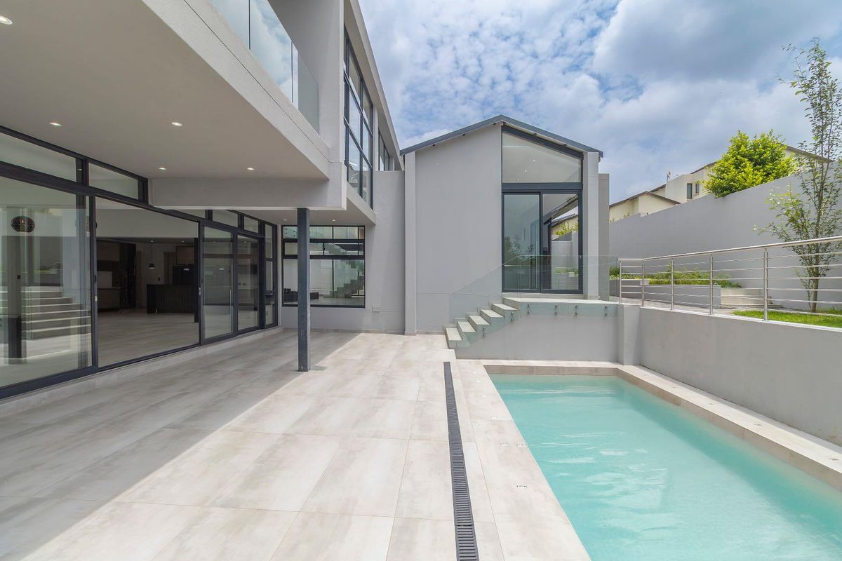 Modern rear exterior featuring a covered patio, swimming pool with glass balustrades, and large sliding glass doors leading into the open-plan living area.