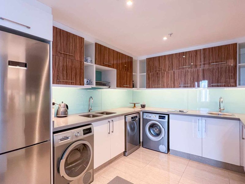 Modern kitchen featuring high-gloss cabinetry, stone countertops, glass splashbacks, and integrated stainless steel appliances including a washing machine and dishwasher.