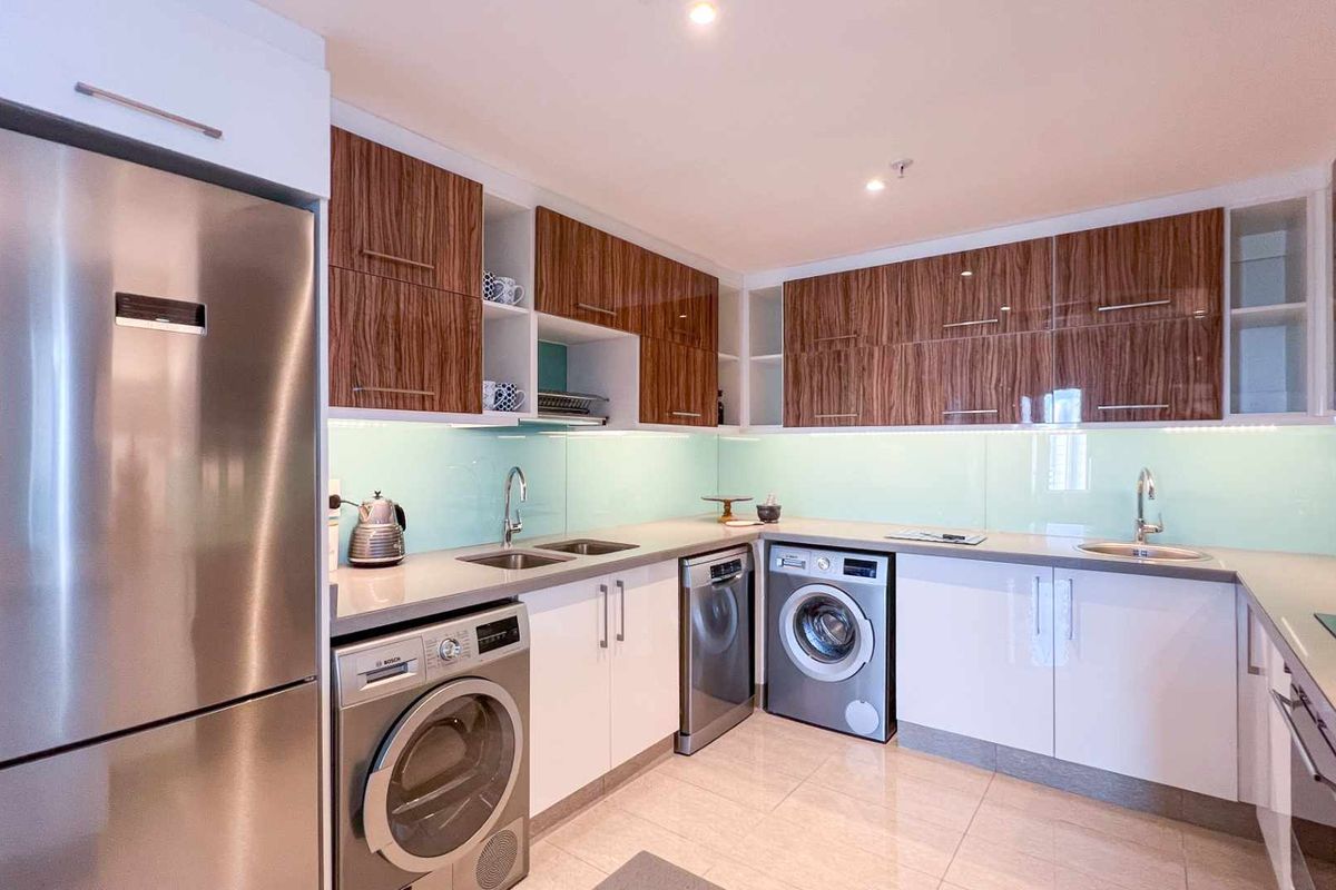 Modern kitchen featuring high-gloss cabinetry, stone countertops, glass splashbacks, and integrated stainless steel appliances including a washing machine and dishwasher.