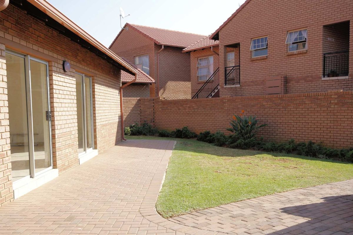 A private rear courtyard featuring a paved patio area, a small lawn, and brick boundary walls, accessible via sliding glass doors.