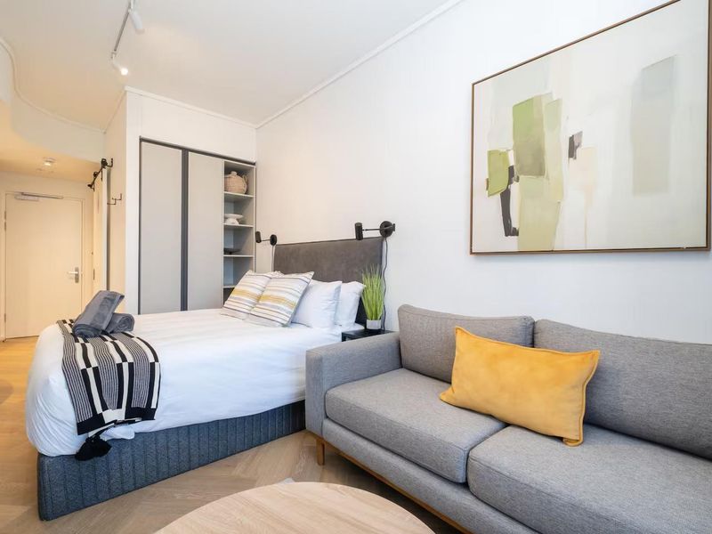 A modern open-plan studio apartment featuring light herringbone timber flooring, built-in wardrobe storage, and contemporary track lighting.