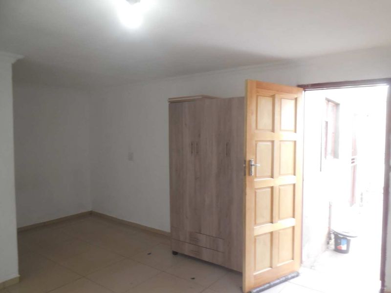 A simple, empty bedroom featuring tiled flooring and a built-in cupboard, with direct access to an outdoor area.