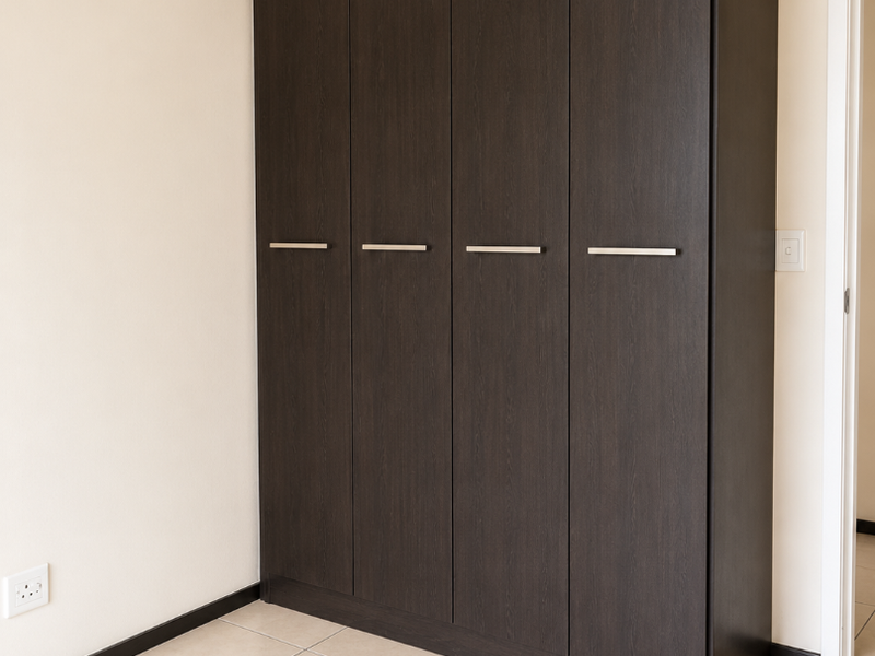 A clean, empty bedroom featuring a modern dark wood built-in wardrobe and neutral tiled flooring.