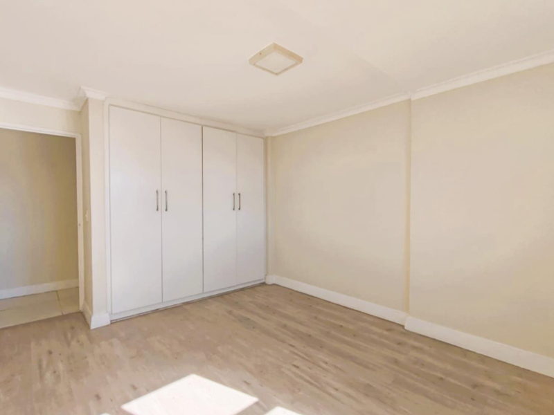 A bright, empty bedroom featuring neutral walls, modern laminate flooring, and ample built-in cupboard storage.