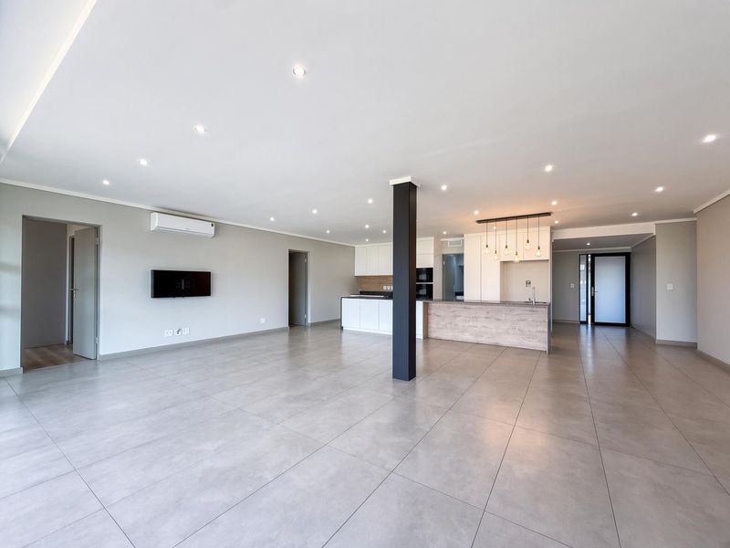 Spacious open-plan living and kitchen area featuring modern tiled flooring, recessed lighting, a central support column, and a contemporary kitchen with built-in cabinetry.