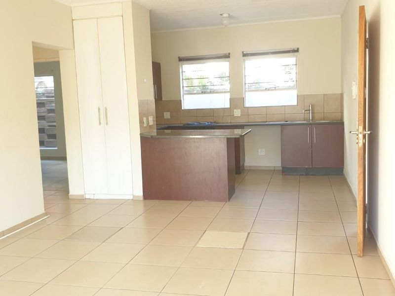 An open-plan living and kitchen area featuring tiled flooring, built-in cabinetry, and a functional kitchen layout with a tiled backsplash.