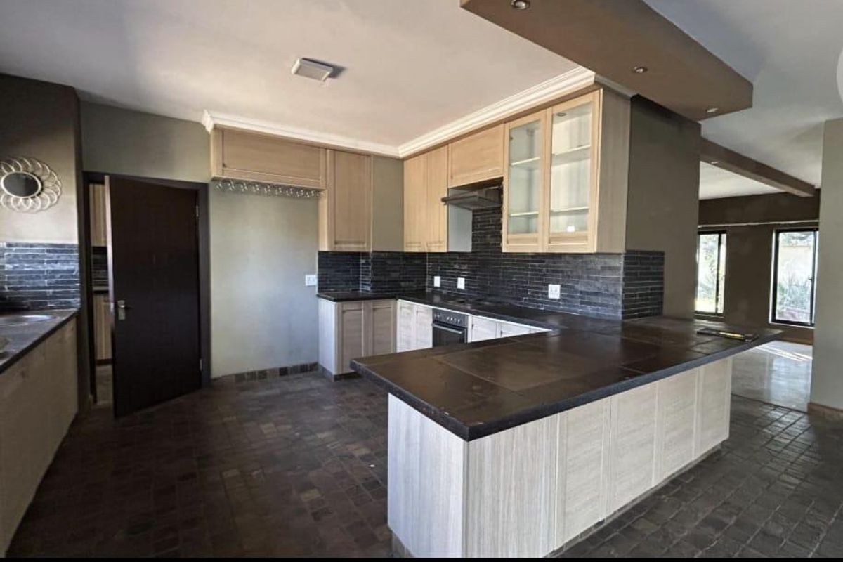 Spacious kitchen featuring light wood cabinetry, dark stone countertops, a tiled backsplash, and a functional layout with a breakfast bar.