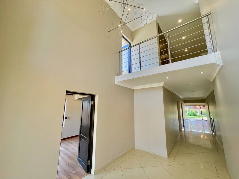 Spacious double-volume entrance hall featuring tiled flooring, recessed lighting, and a modern stainless steel balustrade overlooking the landing.