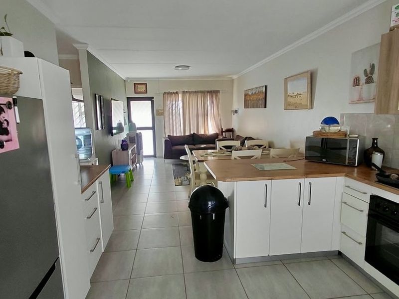 Open-plan living and kitchen area featuring white cabinetry, wooden countertops, built-in oven, and neutral ceramic floor tiles throughout the space.