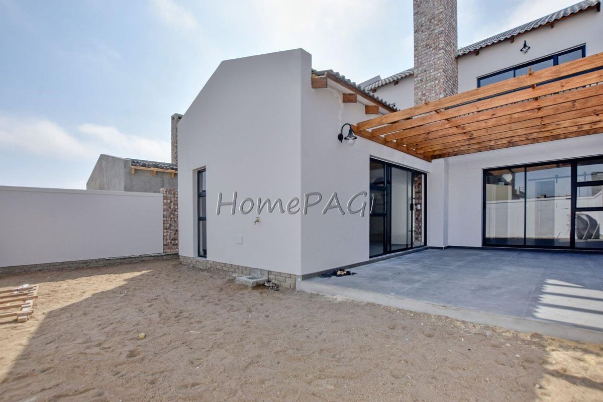 Rear view of the townhouse featuring a tiled patio with a timber pergola, sliding glass doors, and an unfinished garden area.