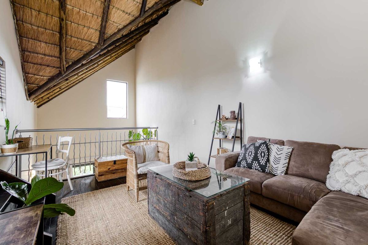 A cozy living area featuring a high vaulted thatched ceiling, exposed timber beams, and a metal balustrade overlooking the lower level.