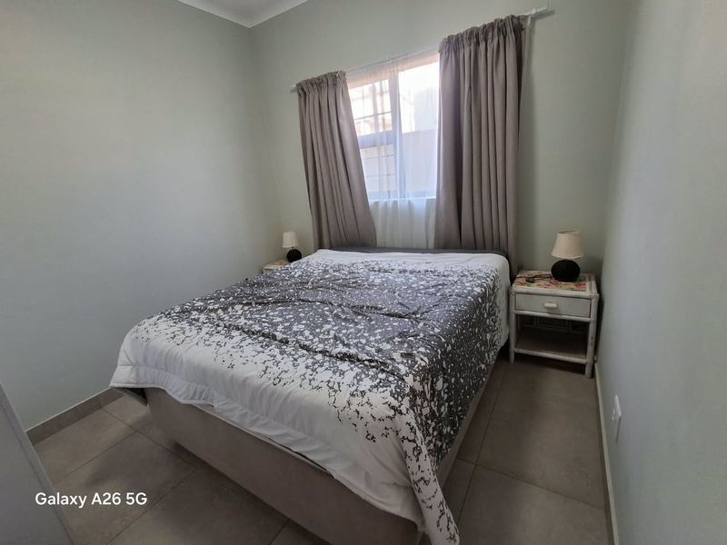 A compact bedroom featuring neutral wall tones, tiled flooring, and a window with installed curtain rails.