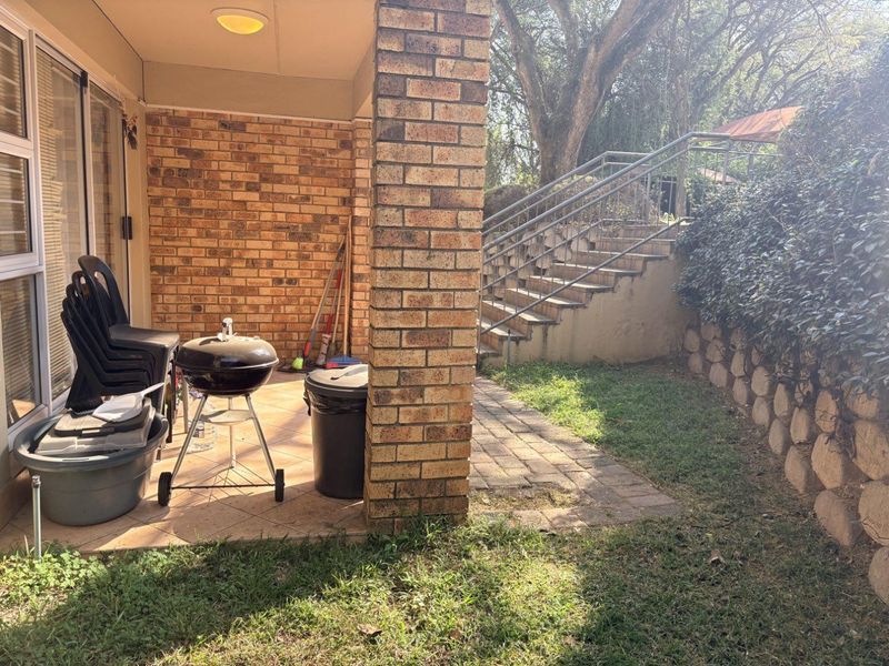 Covered patio area featuring brick construction and tiled flooring, with direct access to a garden space and external staircase.