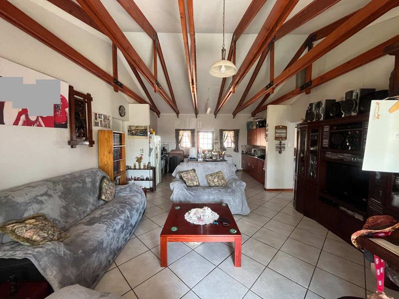 Spacious open-plan living and kitchen area featuring high vaulted ceilings with exposed timber trusses and neutral ceramic floor tiling throughout.