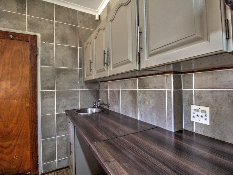 A functional scullery or utility area featuring built-in cabinetry, a laminate countertop, and a stainless steel sink with tiled wall finishes.