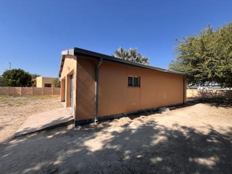 Rear view of the property showing the exterior wall, garage access, and surrounding yard area with a concrete driveway.