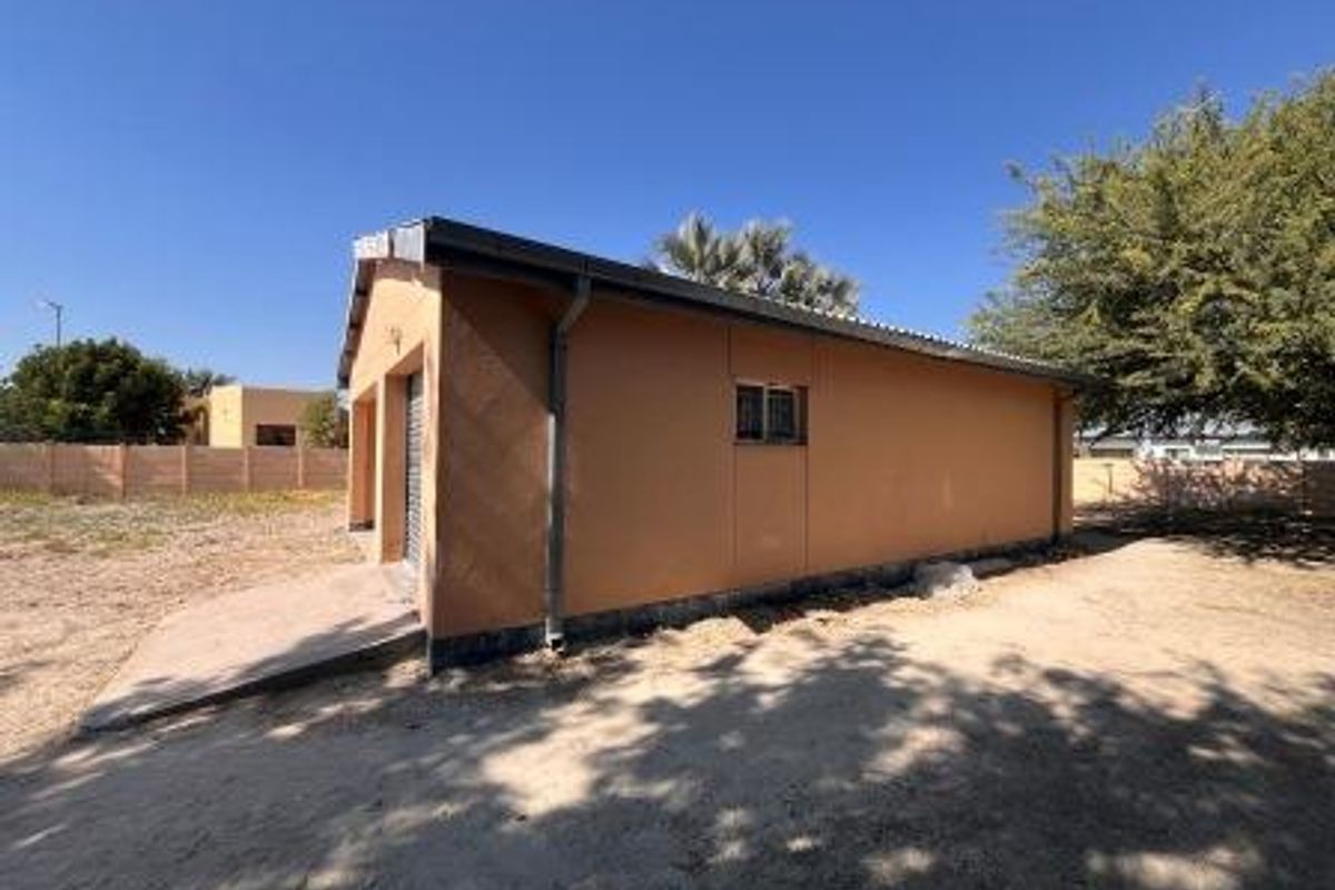 Rear view of the property showing the exterior wall, garage access, and surrounding yard area with a concrete driveway.