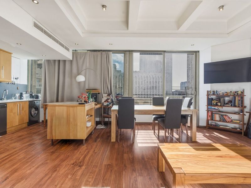 Spacious open-plan living and dining area featuring warm wooden flooring, recessed ceiling lighting, and a functional kitchen with integrated appliances and large sliding glass doors.
