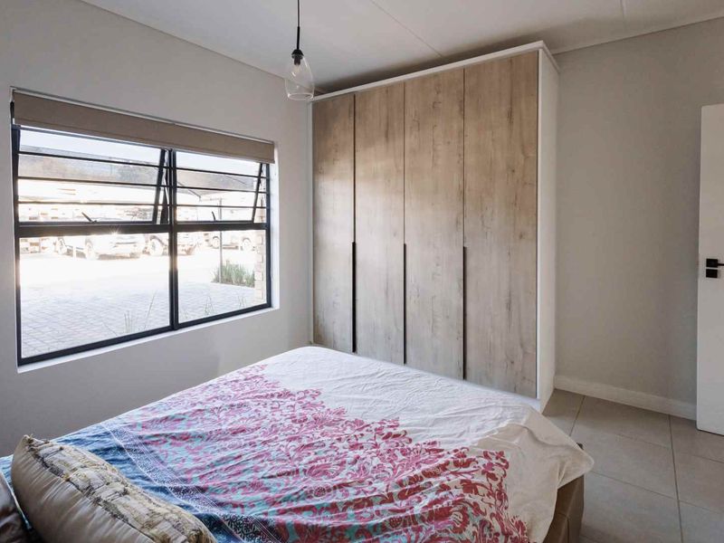 A well-maintained bedroom featuring modern built-in wardrobes, neutral tiled flooring, and a large window with a roller blind for natural light.