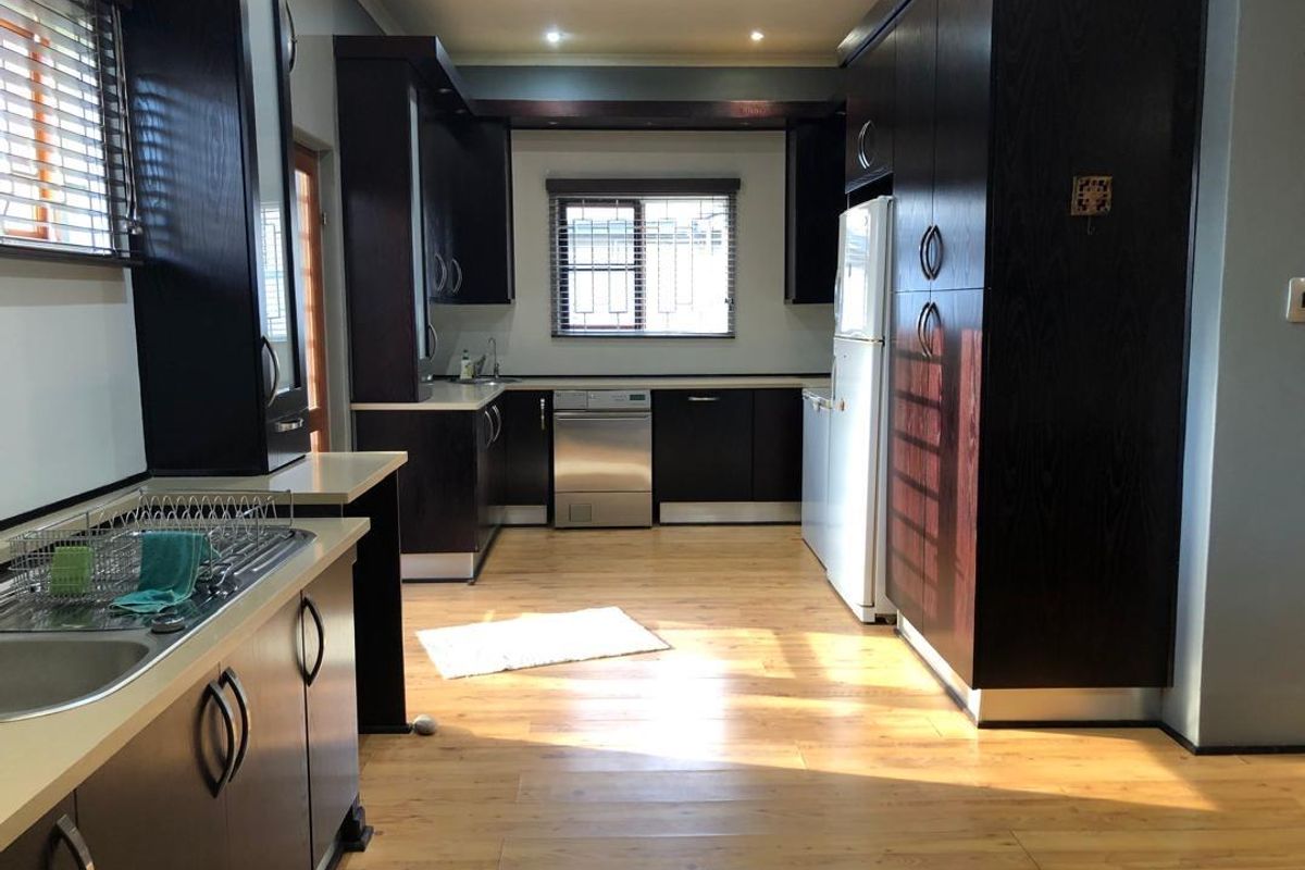 A functional kitchen featuring dark wood cabinetry, laminate countertops, stainless steel dishwasher, and light-toned laminate flooring with ample natural light.